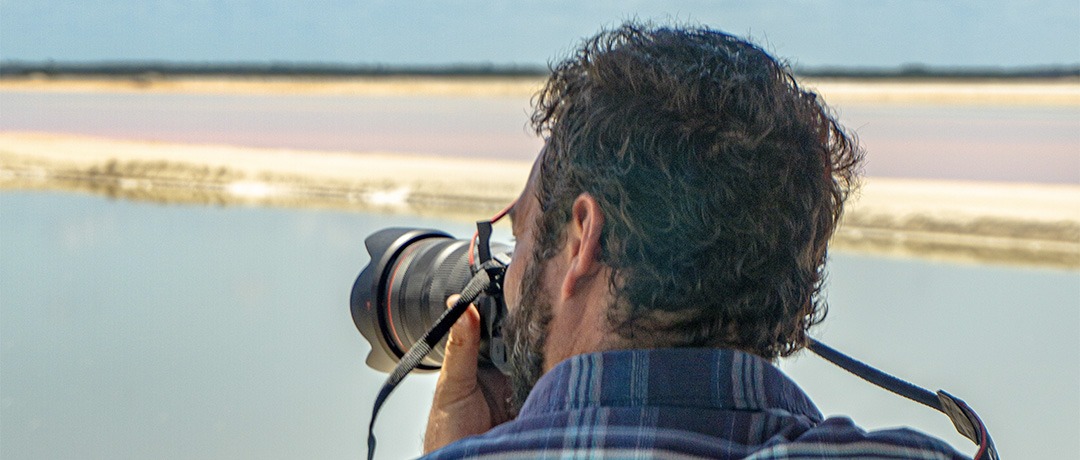 Visitante fotografiando los colores contrastantes de agua rosa, cielo y sal