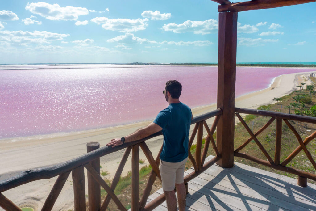 Visitante en Las Coloradas posando, con la laguna rosa de fondo.
